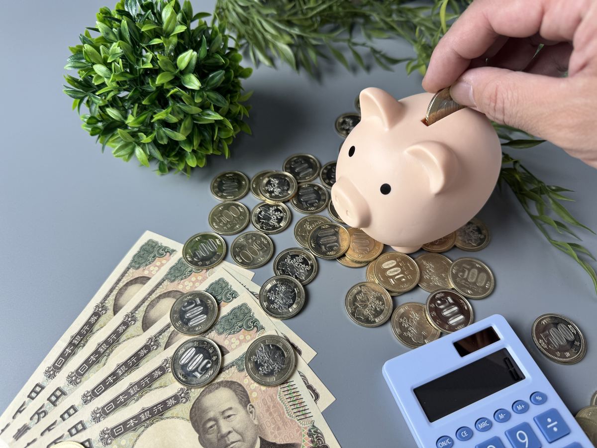 貯金箱に硬貨を入れる手と紙幣。コツコツ積み上がる収益のイメージ